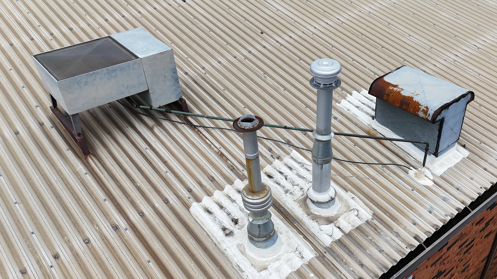 Rooftop exhaust vents and a rust-stained exhaust hood on a corrugated metal commercial roof