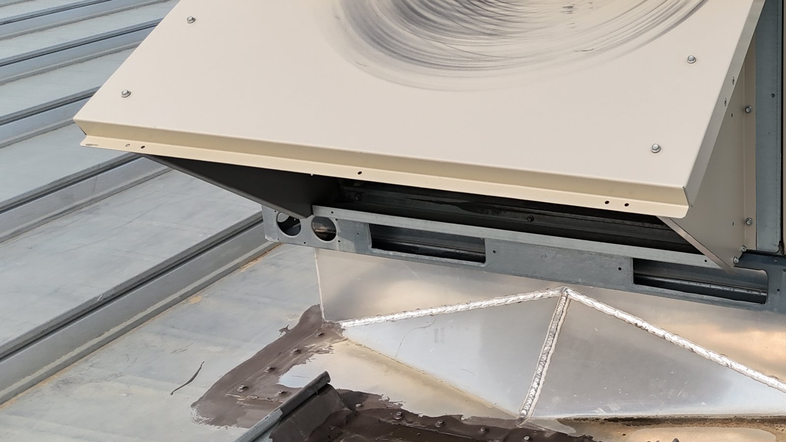 Packaged rooftop HVAC unit on a curb with sealant-patched flashing on a standing-seam metal roof